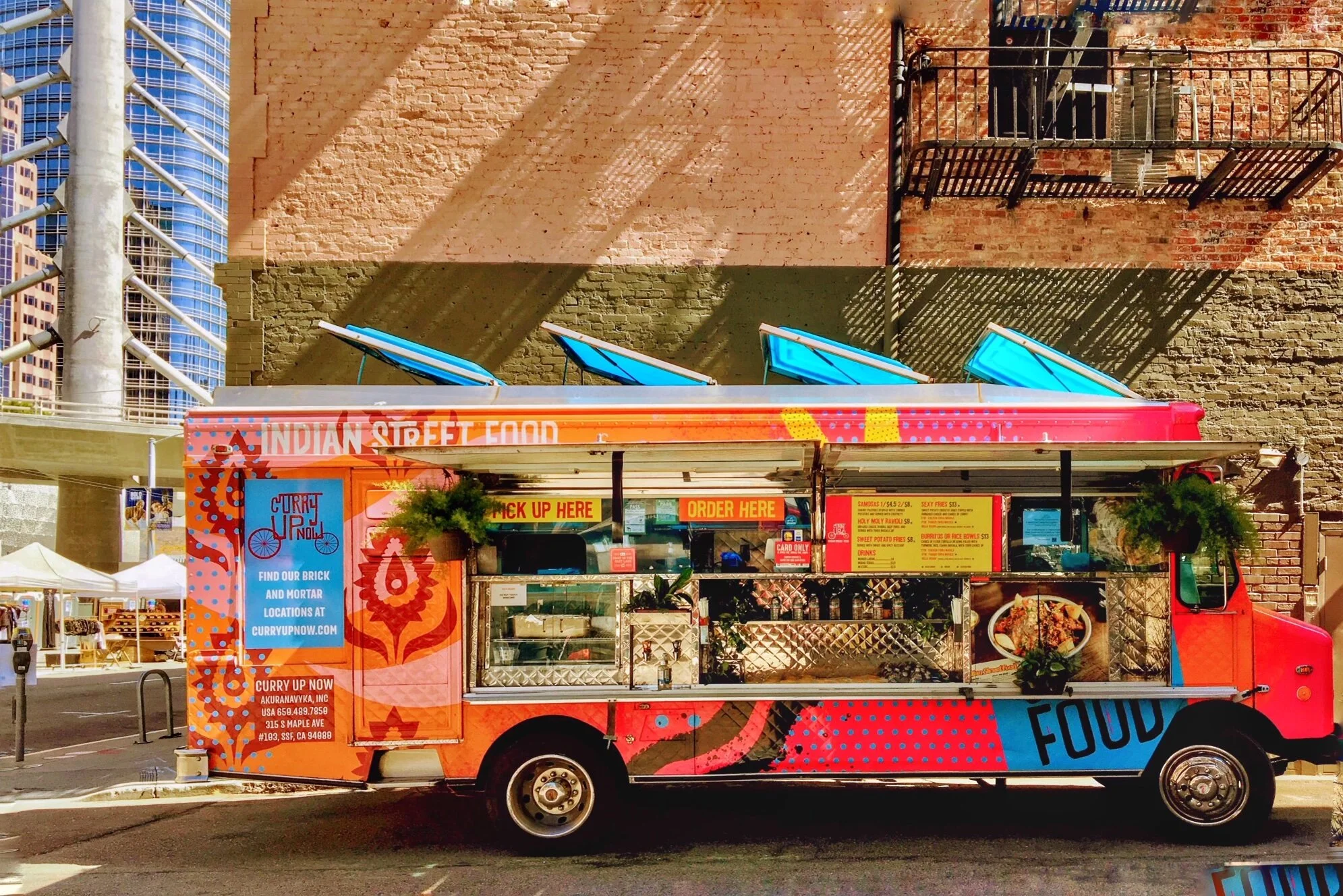 Colorful orange and pink Indian street food truck parked with service windows open and menu displayed.