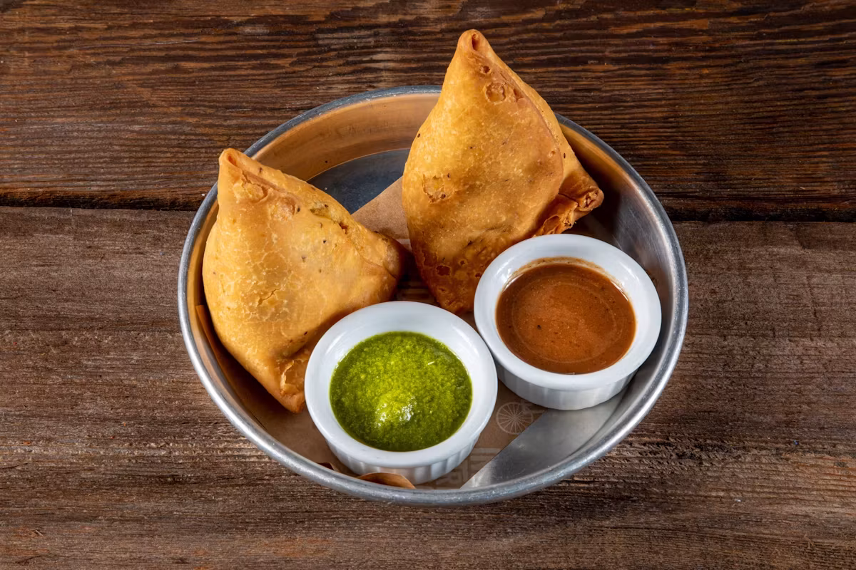 Curry Up Now samosas in a metal bowl with mint and tamarind chutneys
