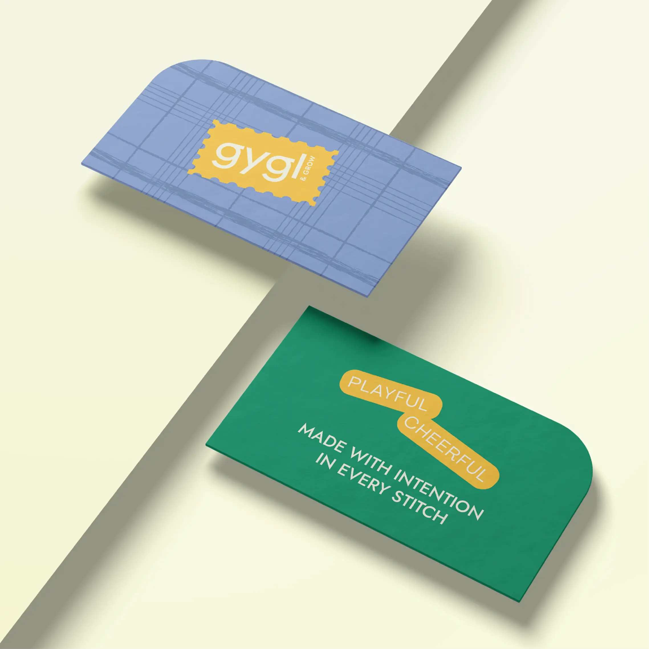 Two clothing tags on a light surface; one blue with a yellow label reading 'gygl & GROW,' the other green with text 'PLAYFUL CHEERFUL MADE WITH INTENTION IN EVERY STITCH.'
