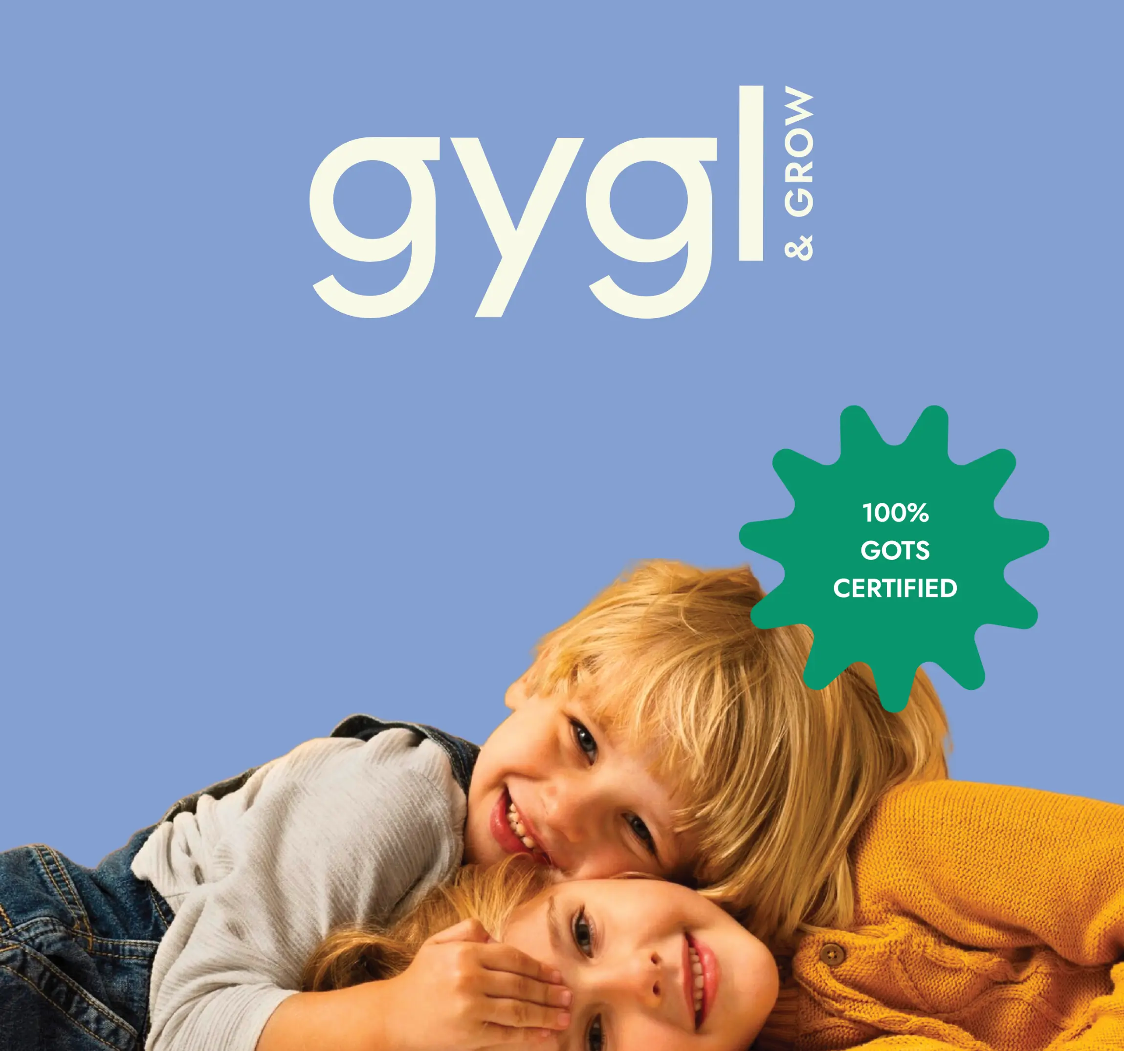 Two smiling young children lying down, one in a yellow sweater and the other hugging from behind, with 'gygl & GROW' text and a green badge stating '100% GOTS CERTIFIED' on a blue background.