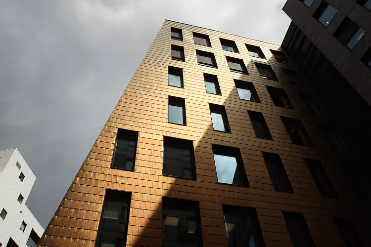 Moderne bygning med kobberfarget fasade og mørke vinduer under en overskyet himmel.