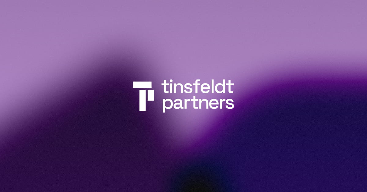 Smilende mand i sort blazer og hvid t-shirt, der kigger ud ad et vindue med sin refleksion synlig.