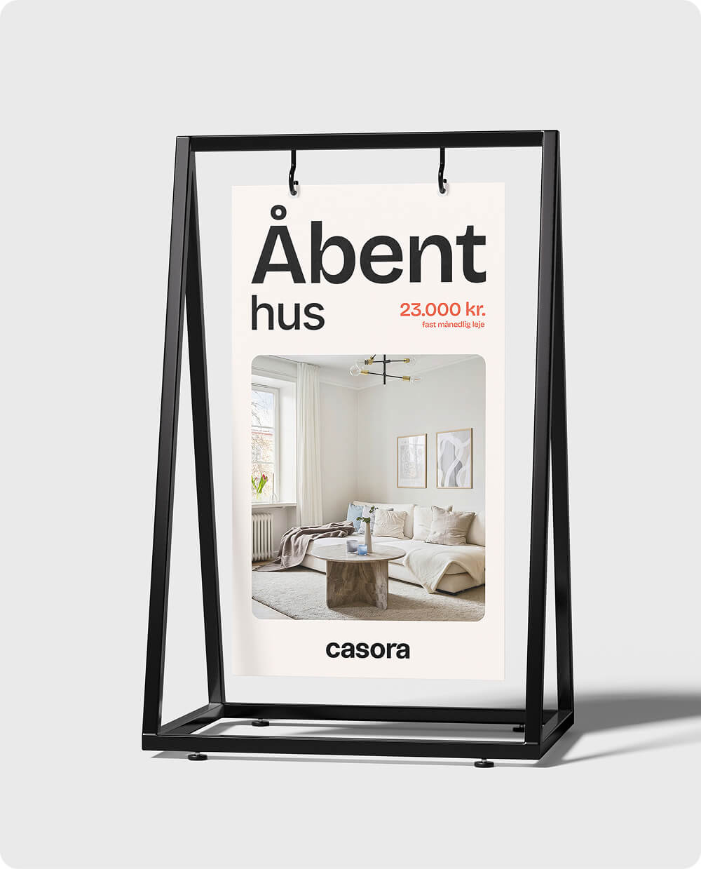 Plakat på sort stander med tekst 'Åbent hus' og billede af moderne stue med hvid sofa og rundt sofabord.
