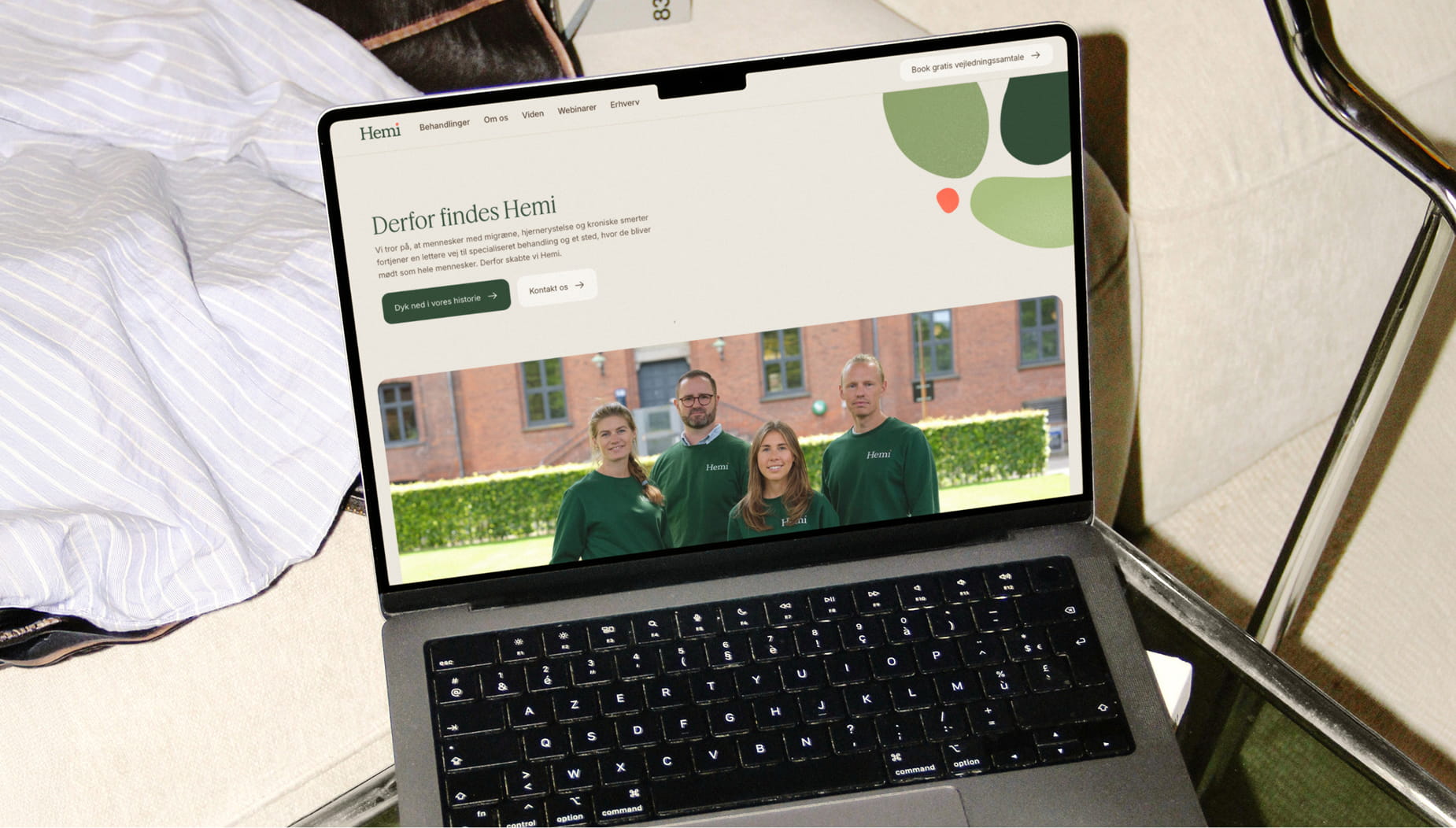 Laptop der viser Hemi Healths website med teamet i grønne trøjer foran en murstensbygning.