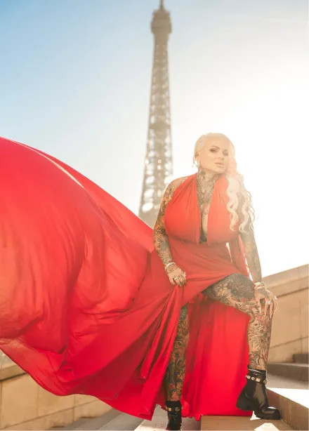 Woman with tattoos wearing a flowing red dress posing on stairs with the Eiffel Tower in the background.