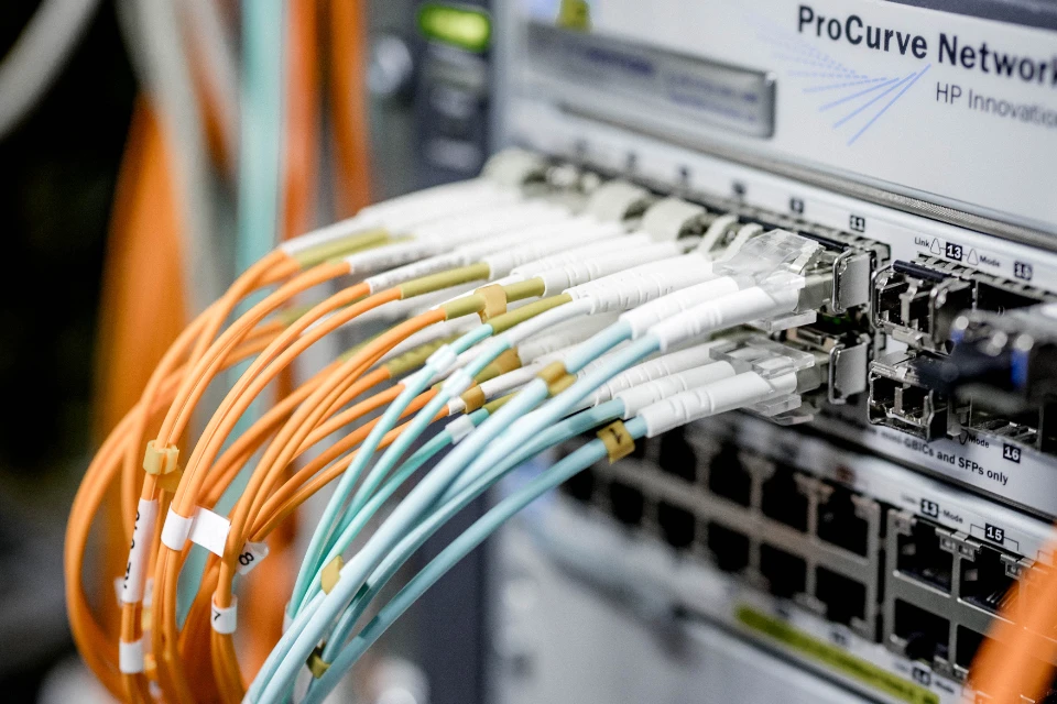 Verschiedene Glasfaserkabel in Orange und Hellblau sind in einen Netzwerk-Switch eingesteckt.