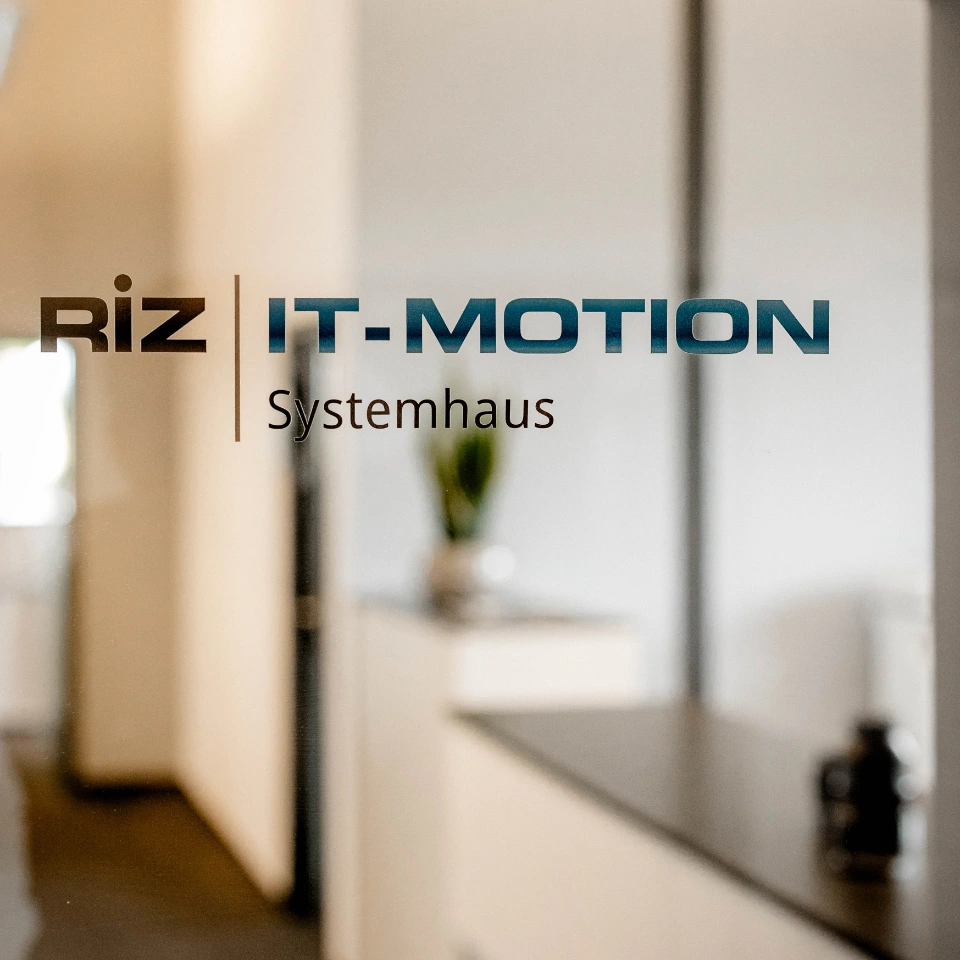 Eingangstür mit dem Schriftzug RiZ IT-MOTION Systemhaus vor einem modernen Empfangsbereich.