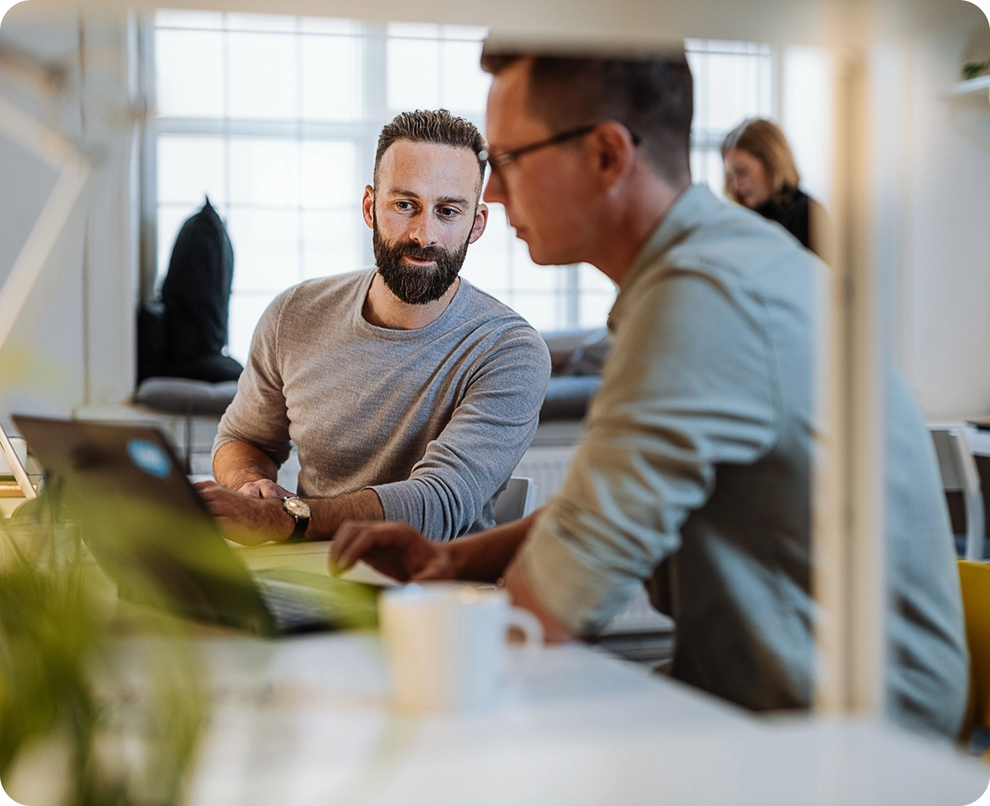 Twee mannen werken samen aan een laptop in een modern, licht kantoor.