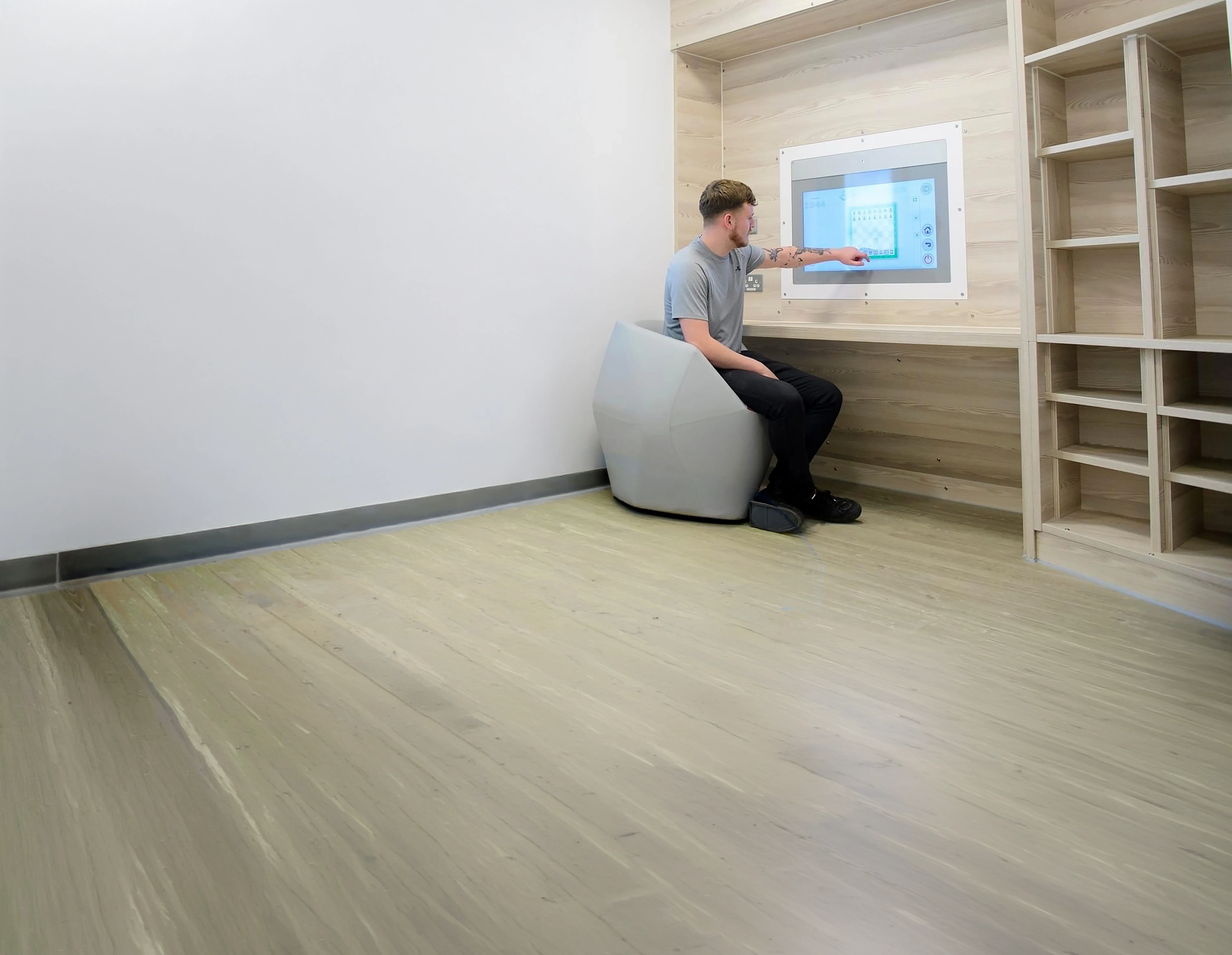 Man zittend op een moderne stoel wijst naar een groot scherm in een minimalistisch houten interieur.