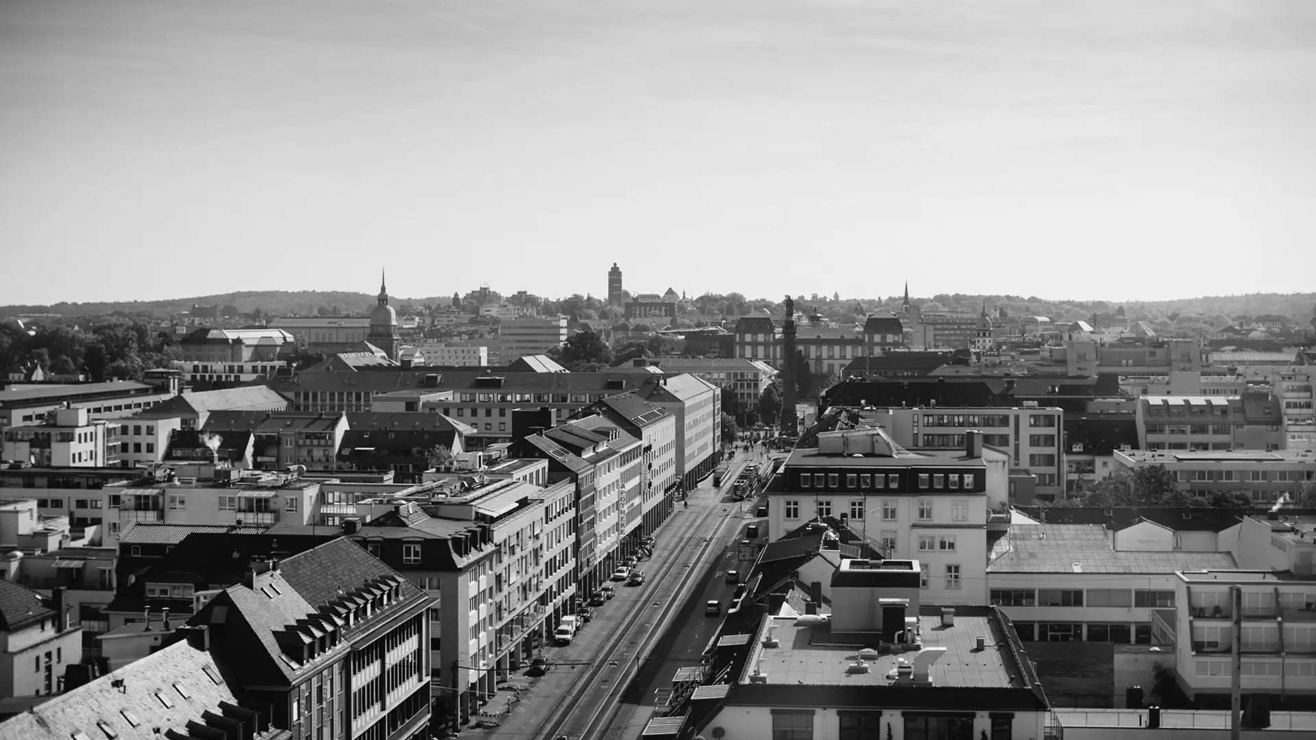 Black and white aerial view of a city street lined with buildings and a distant tower under a clear sky.
