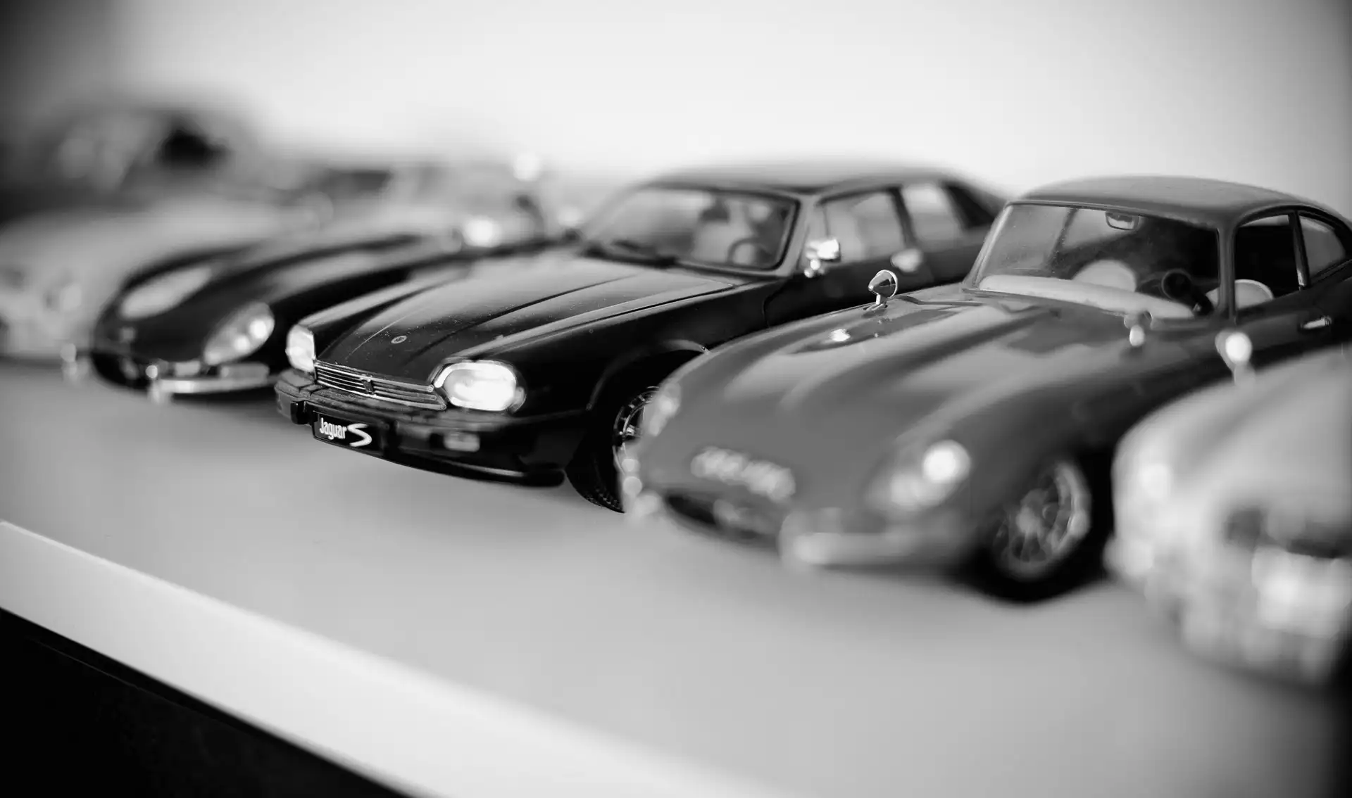 Close-up of a row of detailed model cars displayed on a white surface in black and white.