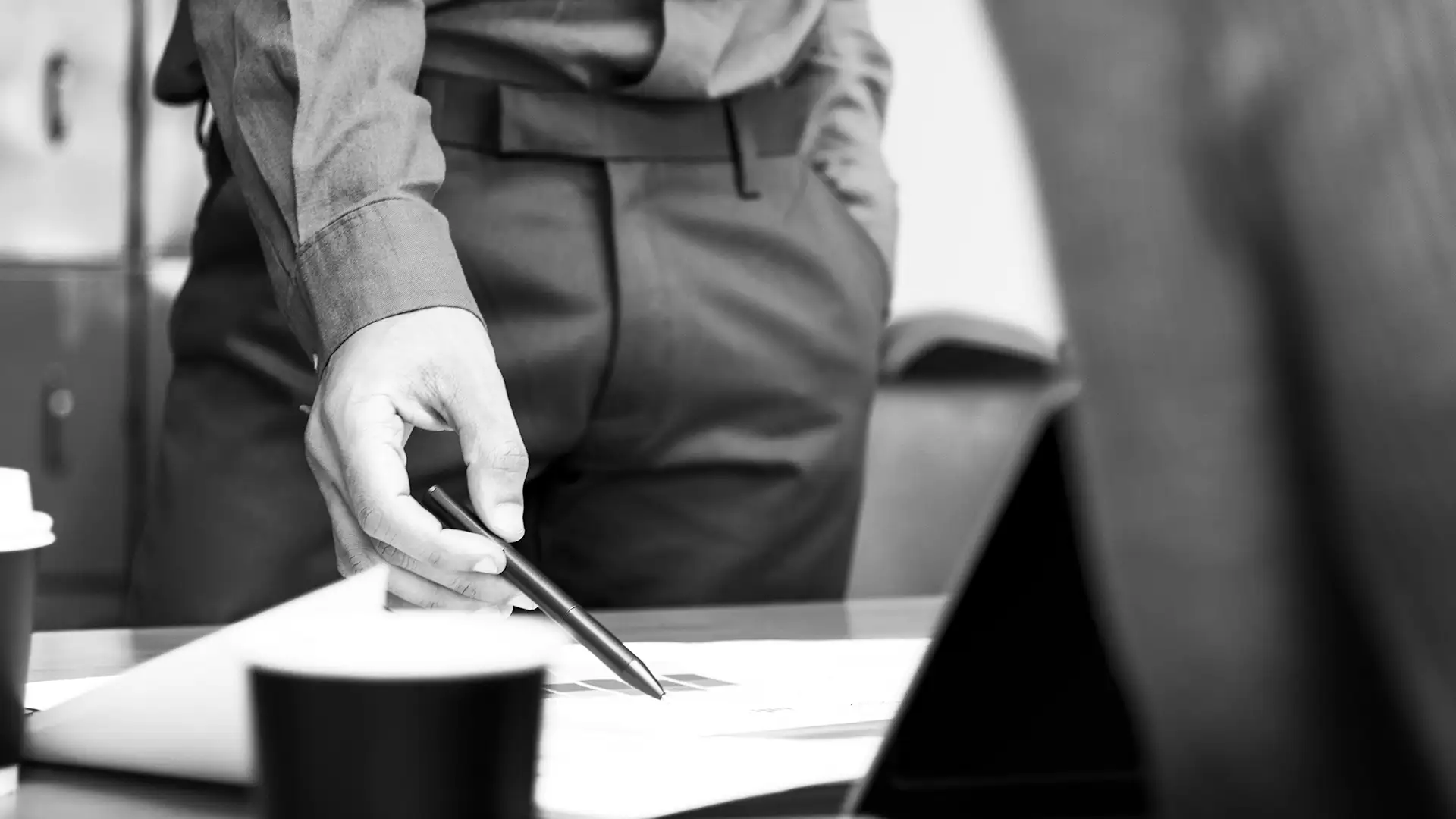 Man in business attire pointing at documents on a table with a pen during a meeting.