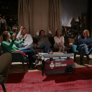 Escape game Apéro locked box 
Cinq personnes assises dans un salon discutent, avec une glacière rouge Igloo au centre sur un tapis rouge.