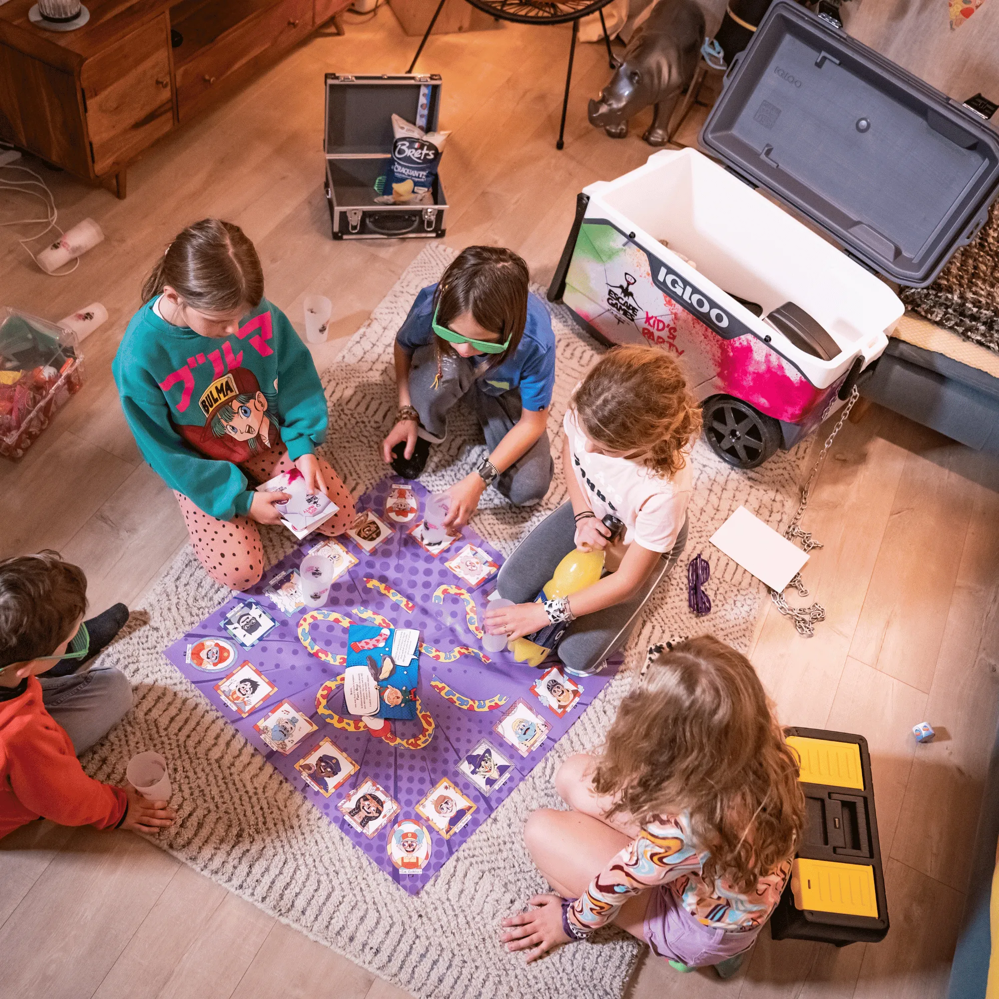 Quatre enfants jouent sur un tapis avec un jeu de société coloré représentant divers personnages, entourés de divers objets dans une pièce. escape game kids