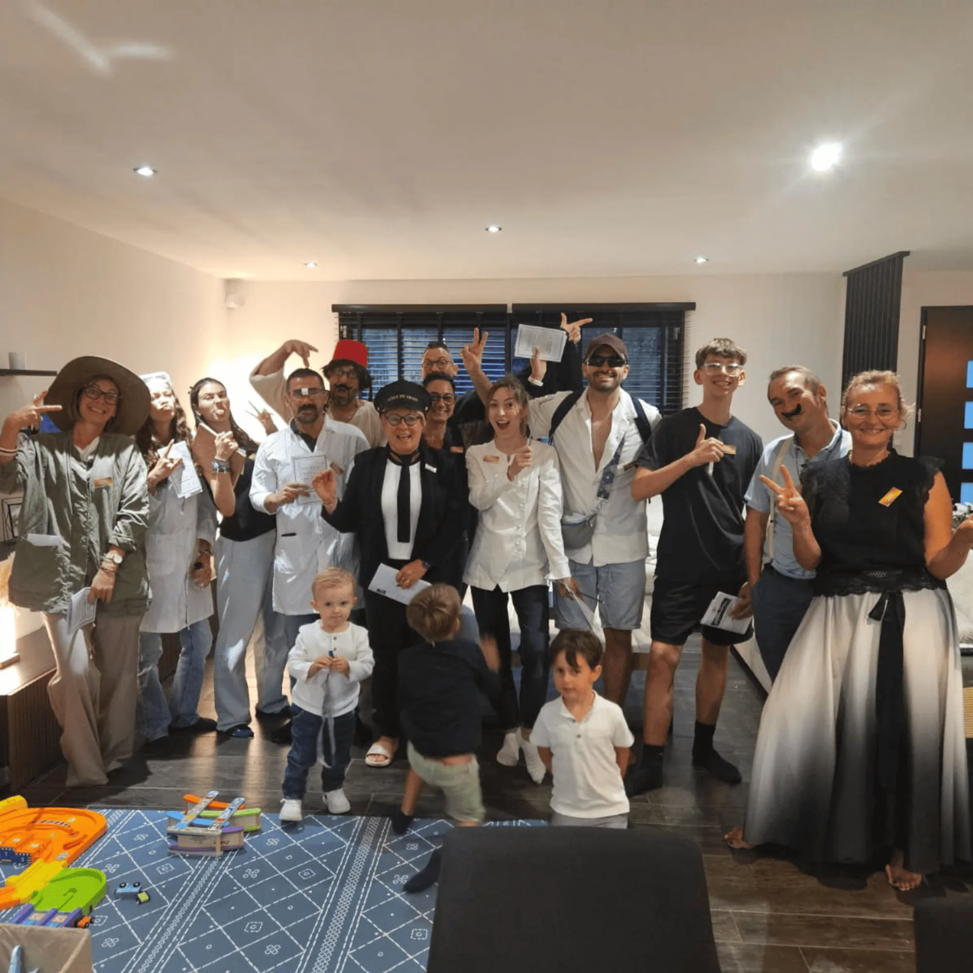 Groupe joyeux de vingt personnes, adultes et enfants, posant ensemble dans une pièce bien éclairée avec un tapis et des jouets au sol. murder party