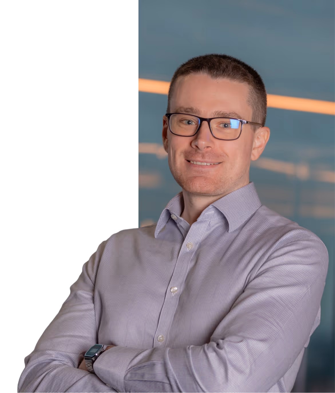 Smiling man with short hair and glasses, wearing a light purple button-up shirt with arms crossed.
