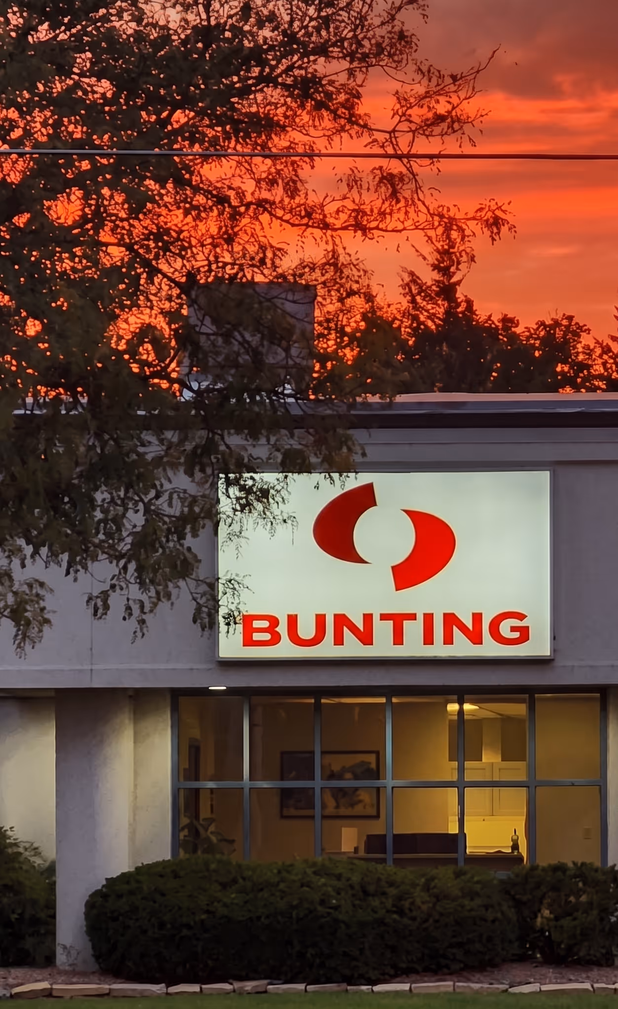 Building exterior with illuminated Bunting company sign under an orange sunset sky.