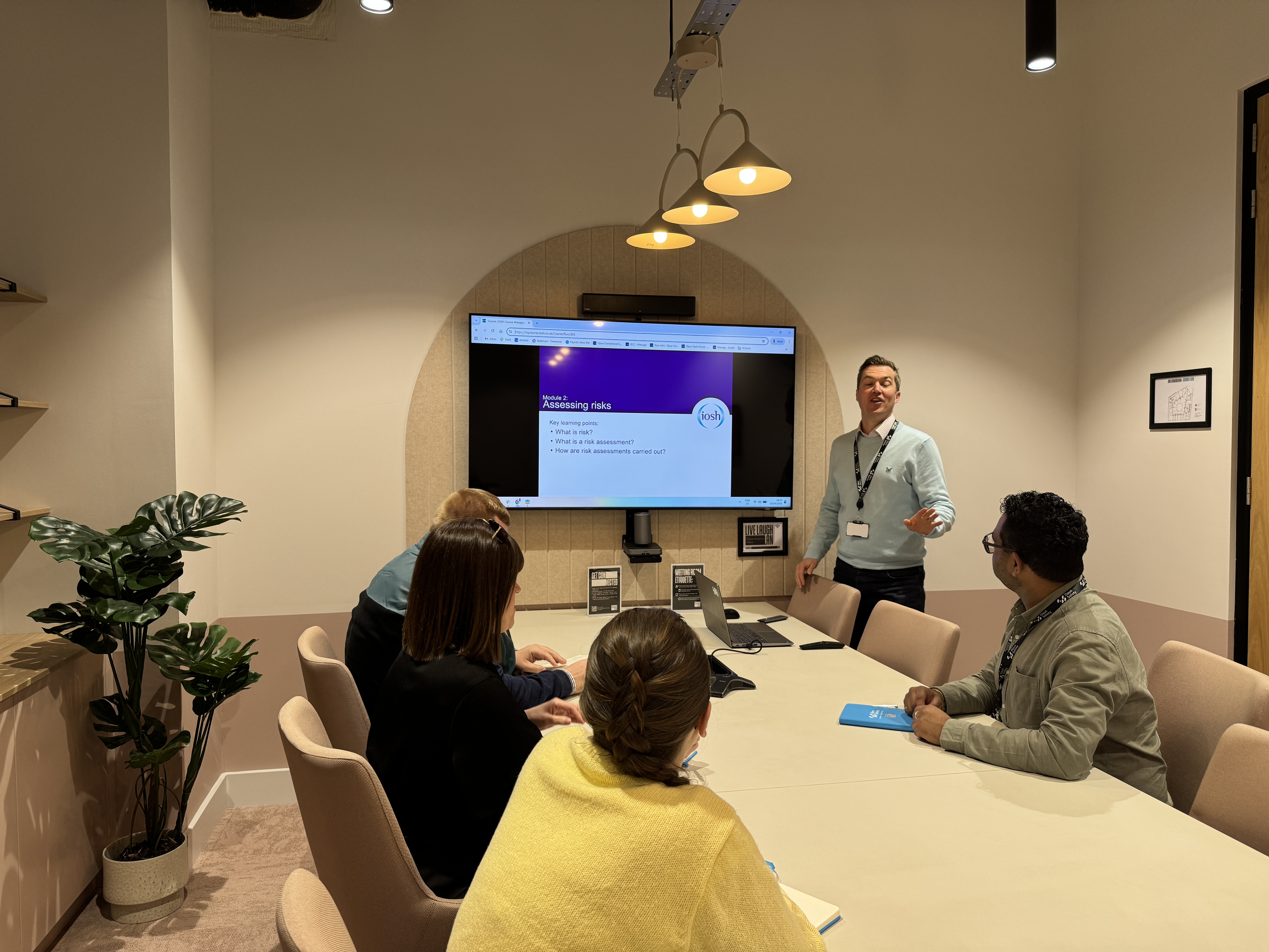 People in a meeting room attending a presentation on risk assessment displayed on a wall-mounted screen.