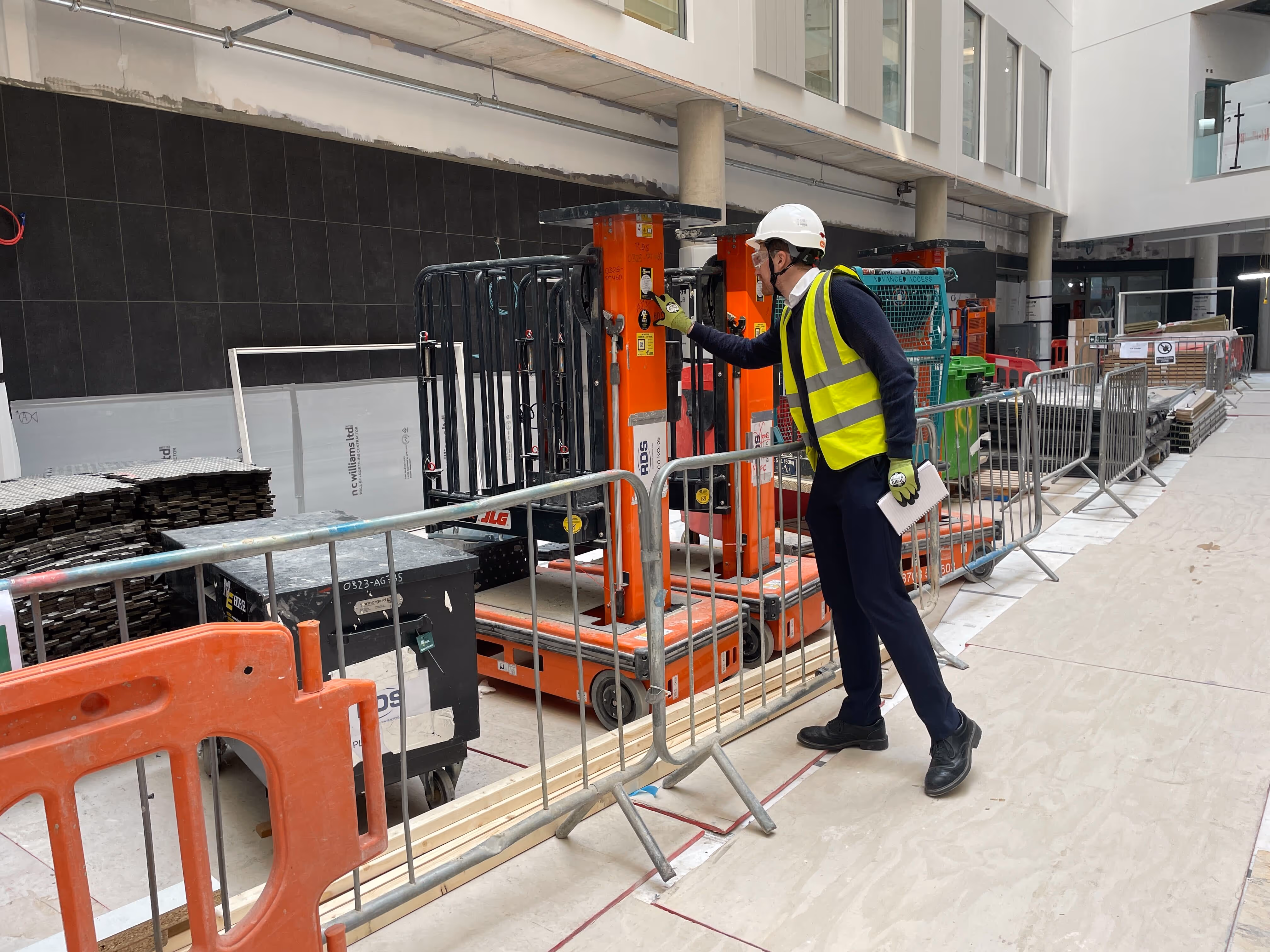 Construction worker in safety gear operating an orange lift inside a building under construction.
