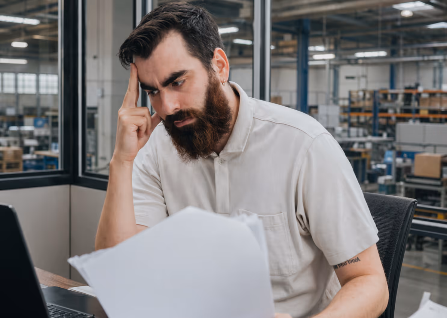 Stressed man at a desk reviewing paperwork in an office setting.