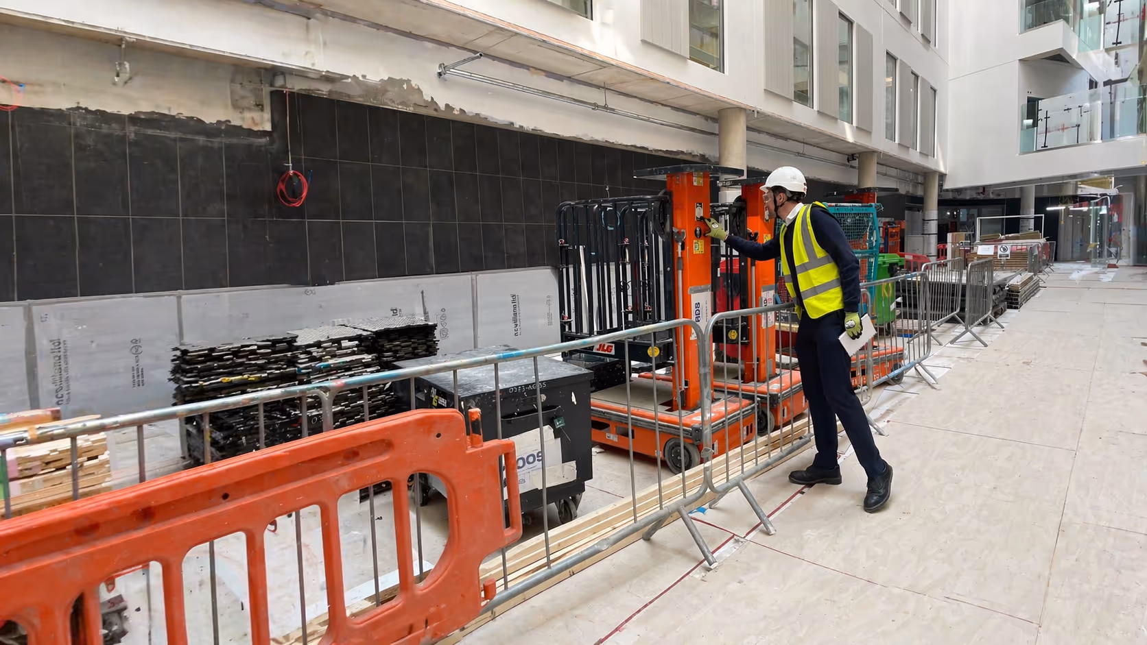 Construction site with workers in safety gear and orange safety barriers.