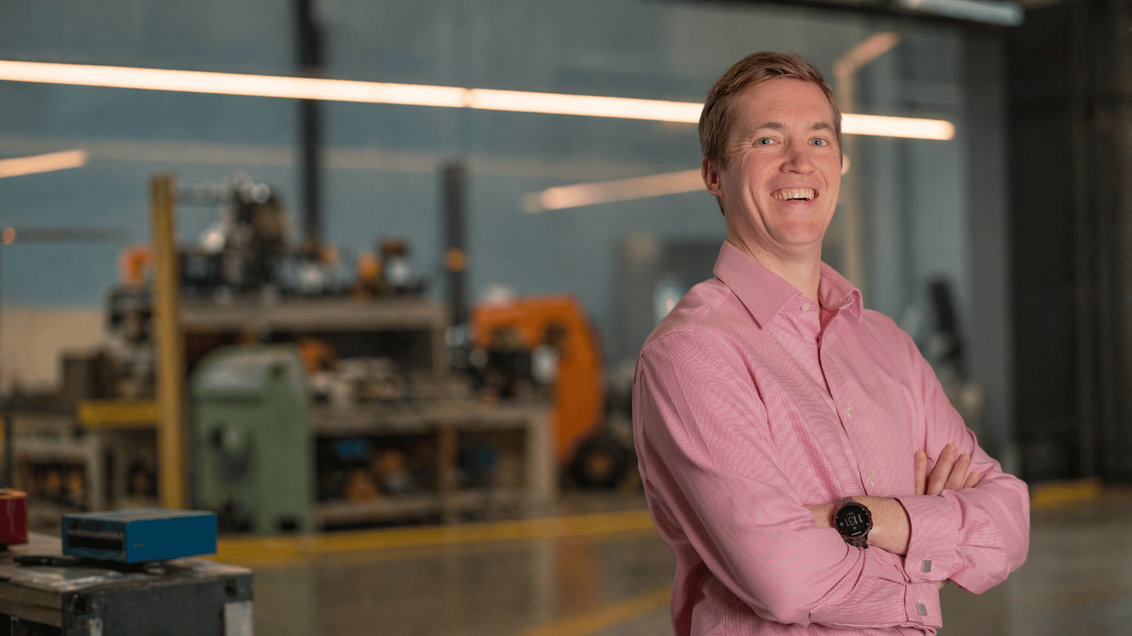 Ian, an Opus Safety team member, smiling with arms crossed in a workshop setting.