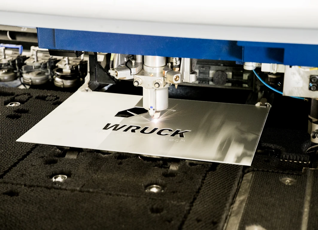 Laser schneidet das Wort WRUCK aus einem Metallblech in einer Industriemaschine.