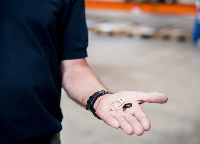 Mann hält kleine Metallteile in seiner Hand in einer Werkstatt oder Industrielumgebung.