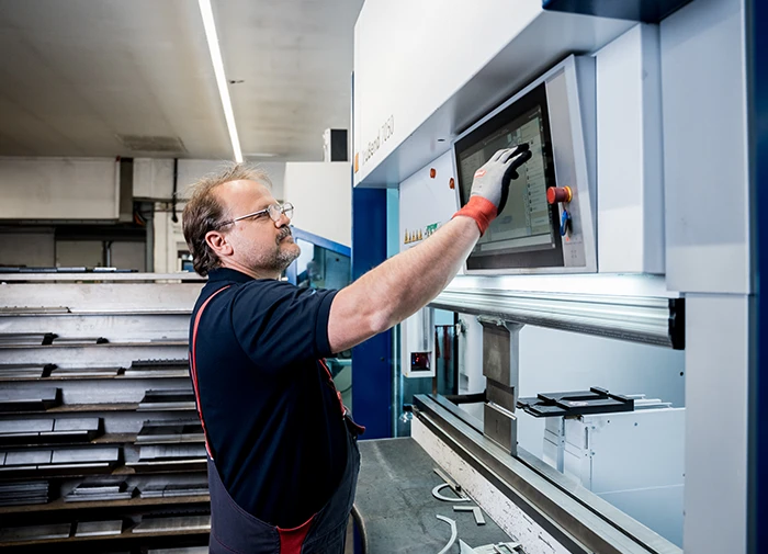 Ein Mann bedient eine CNC-Maschine zur Blechbearbeitung mit einem Touchscreen im Werkstattbereich.