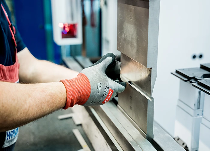 Arbeitshandschuhe führendes Blech in CNC-Biegemaschine während eines Biegens von Metallteilen.