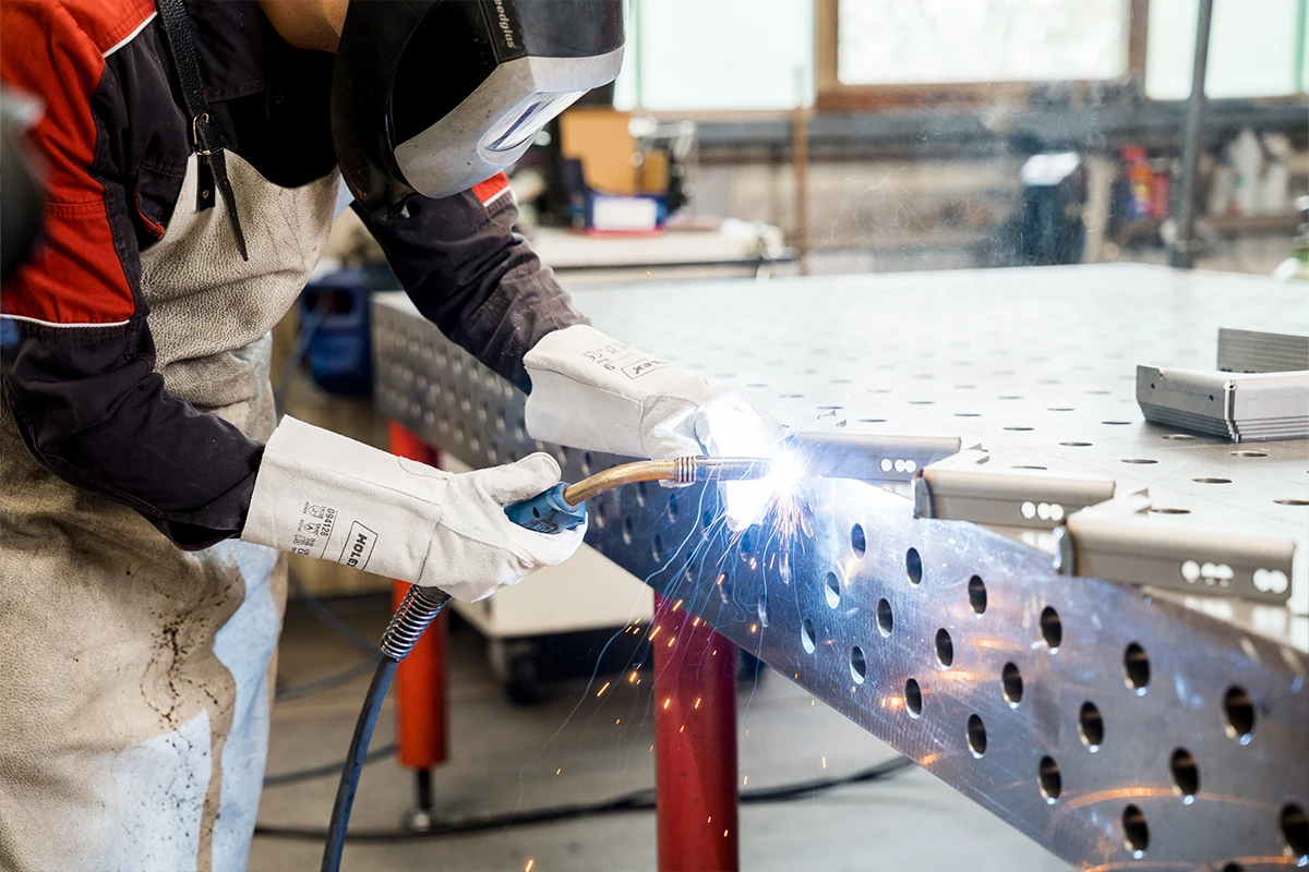 Handwerker schweißt Sicherheitsblech mit Schutzhelm und Handschuhen in Werkstatt.