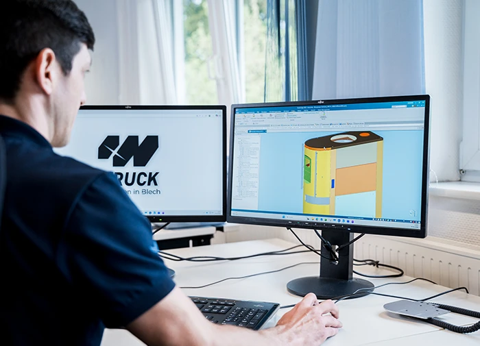Mann arbeitet an dualen Monitoren mit CAD-Software zur Konstruktion eines Gelb-Bauteils.