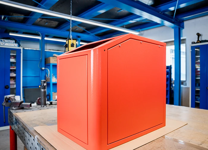 Rotes, pulverbeschichtetes Metallgehäuse in einer blauen Werkstatt auf einem Arbeitstisch.