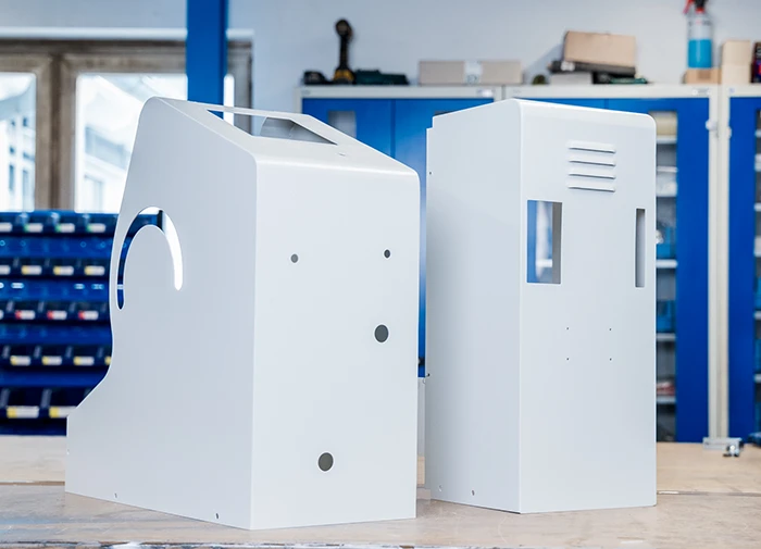 Zwei weiße pulverbeschichtete Metallgehäuse stehen auf einer Werkbank in einer Werkstatt.