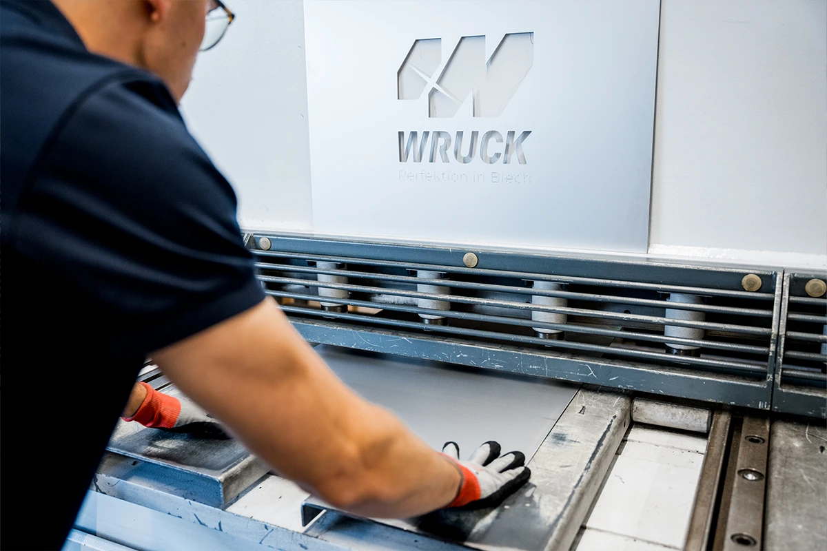 Arbeitskraft in Handschuhen bearbeitet Metallblech an Maschine mit WRUCK-Logo.