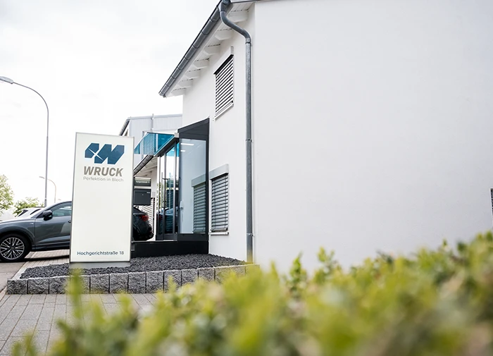 Eingangsbereich eines modernen Bürogebäudes mit WRUCK Firmenschild und Gehweg.