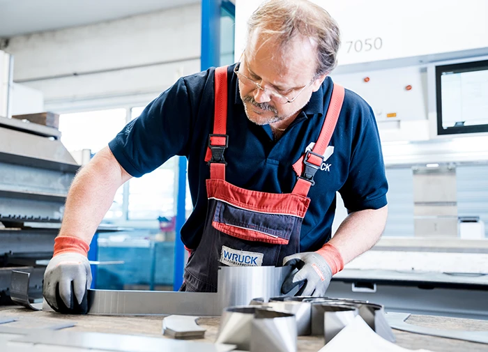 Handwerker in Arbeitskleidung arbeitet präzise an einem Metallstück in einer Werkstatt.