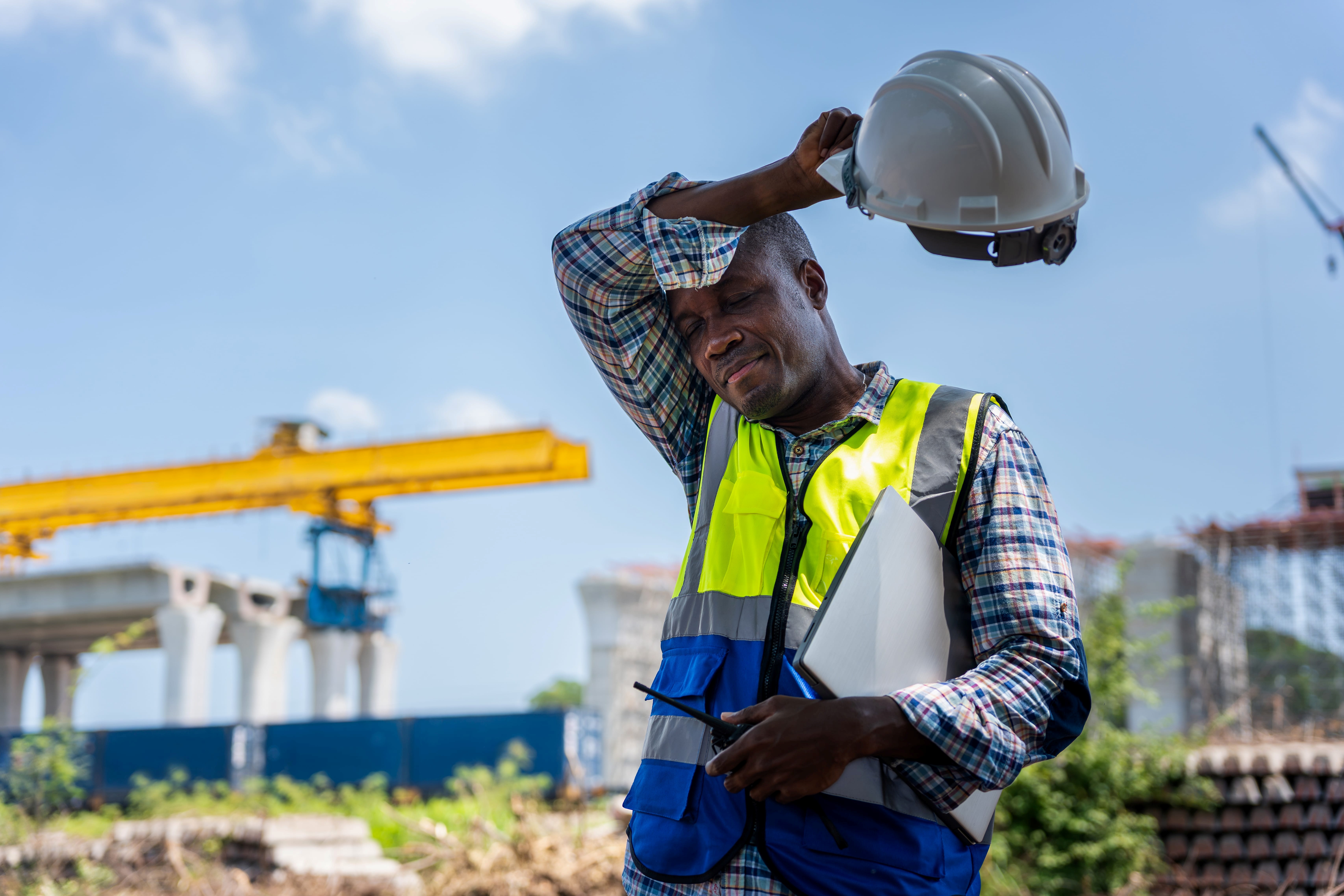 Exhausted construction worker holding his hard hat while taking a break in the heat on site