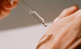 Dropper releasing serum onto the textured skin of a hand.