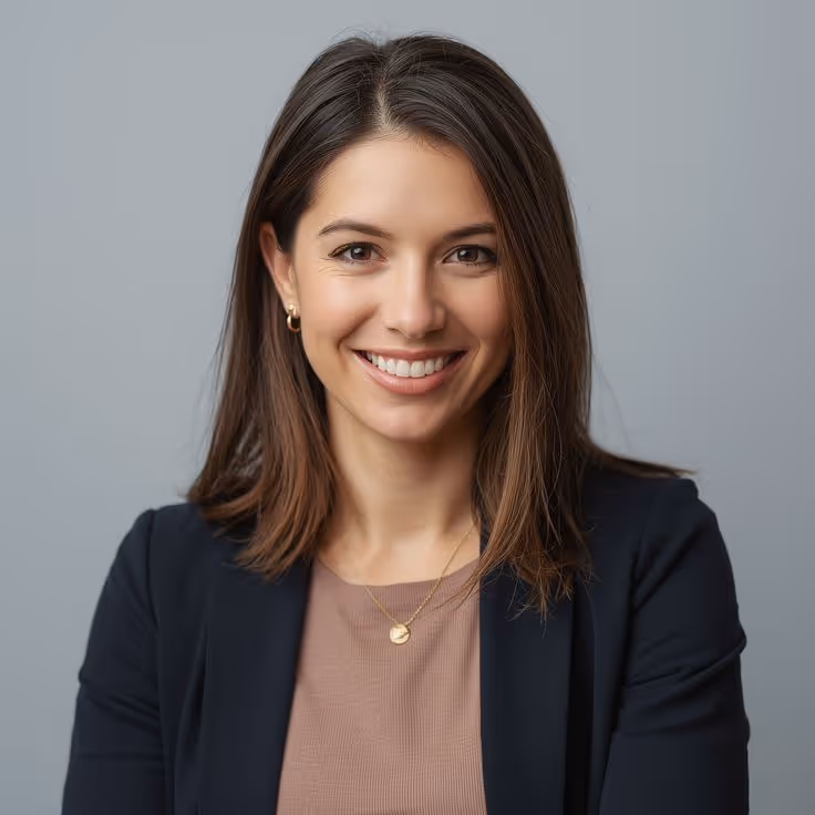 Smiling young woman with straight brown hair wearing a black blazer and beige top against a gray background.