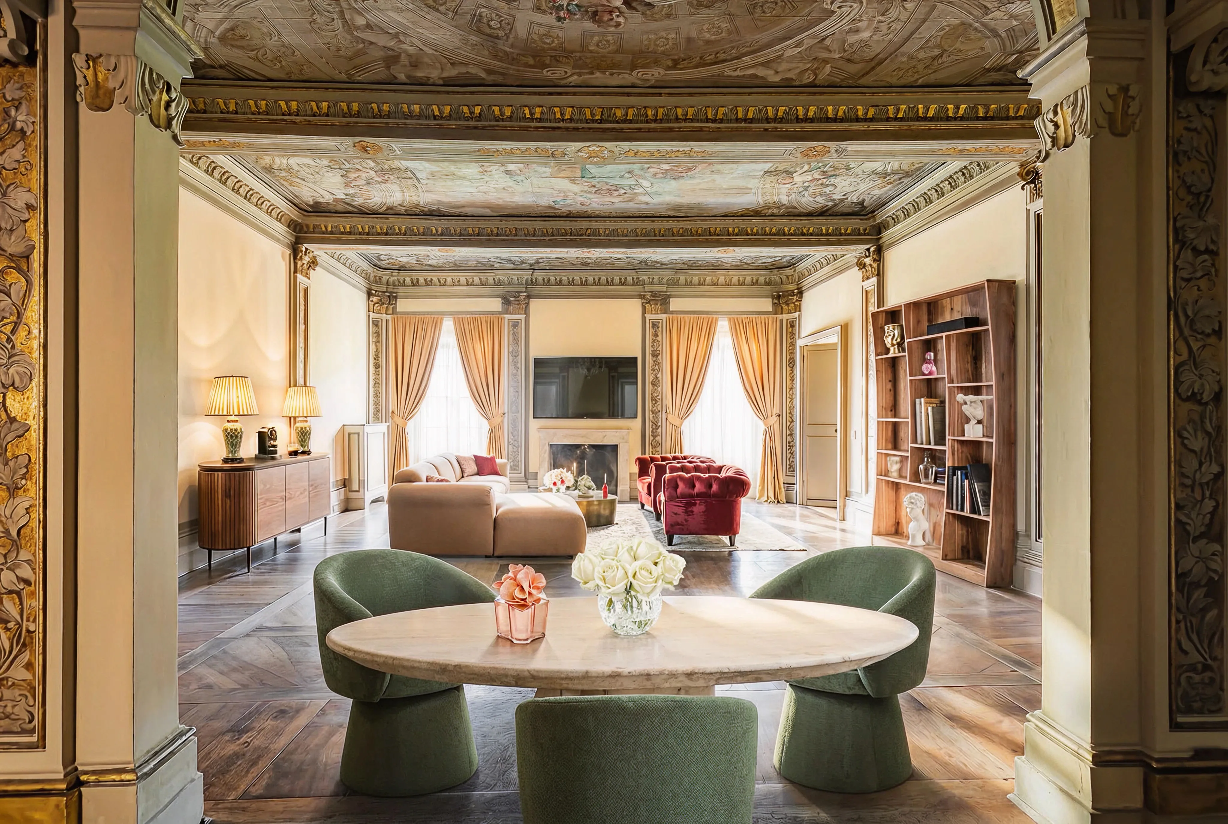 Elegant living room with ornate ceiling, green chairs around a white oval table, beige and red sofas, and large windows with gold curtains.