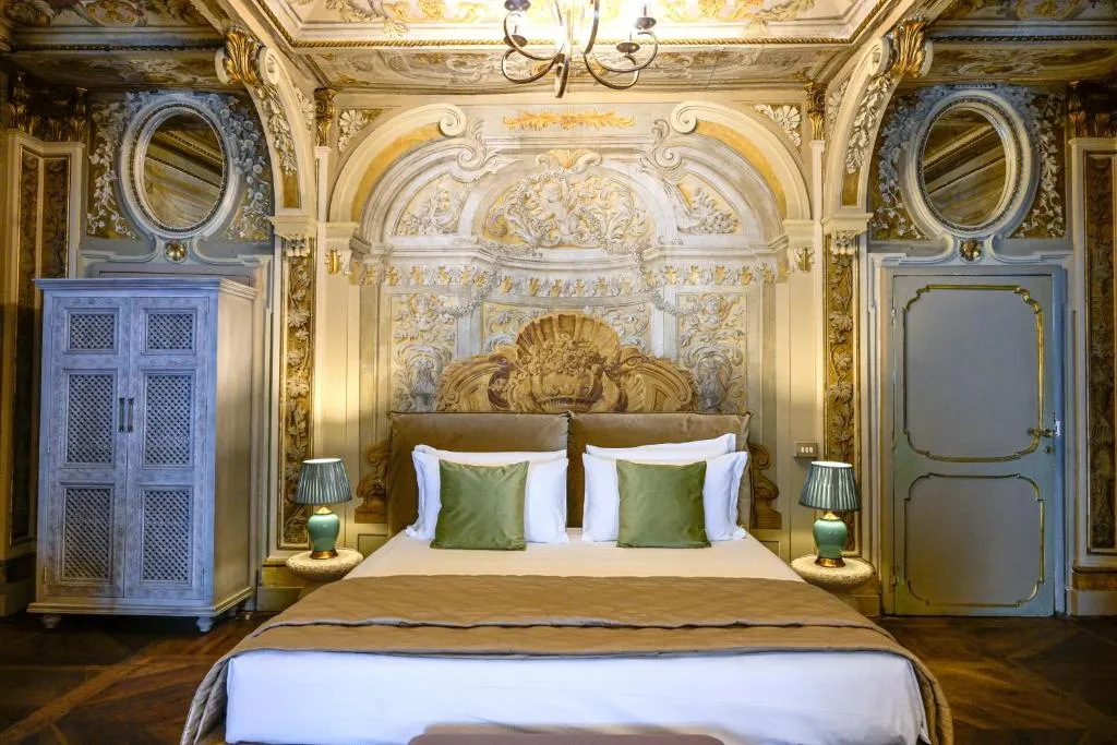Luxurious bedroom with an ornate gold and white baroque headboard, green pillows, two bedside tables with green lamps, and detailed wall and ceiling decorations.