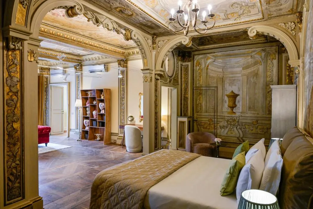Luxurious bedroom with ornate gold-trimmed walls and ceiling, a large bed with green and white pillows, and classic wooden flooring.