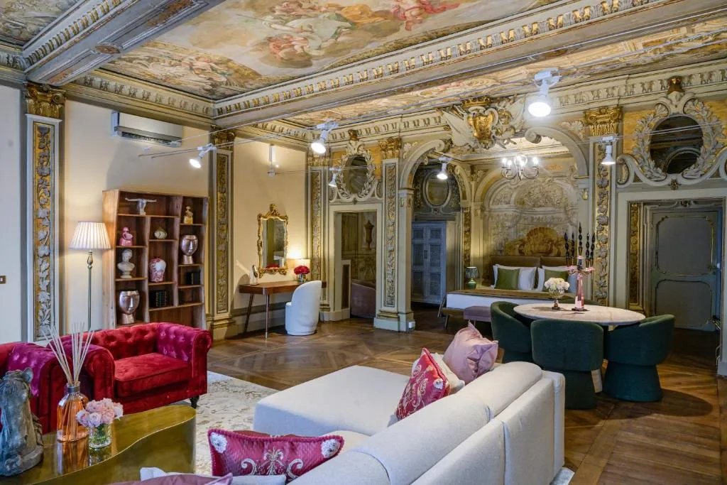 Luxurious living room with a painted ceiling, ornate wall decorations, red velvet armchairs, a beige sectional sofa, and a round dining table with green chairs.