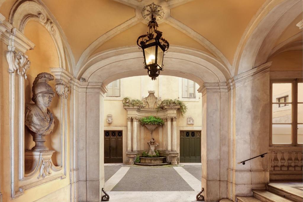 Stone archway leading to a courtyard with a central fountain, a bust sculpture on the left, and a hanging lantern overhead.