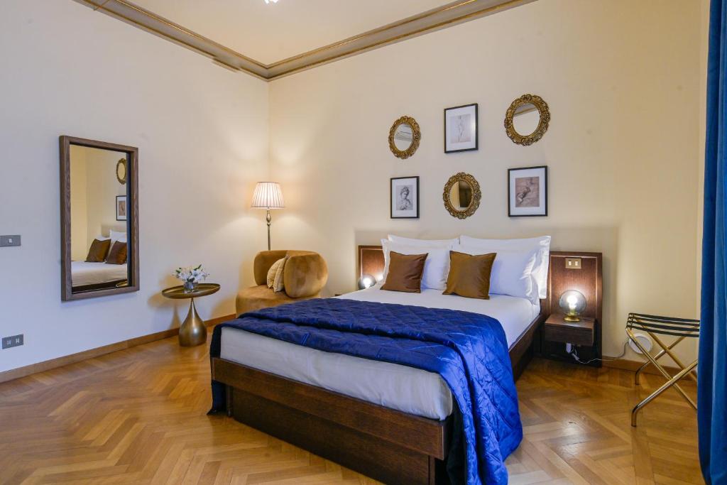 Cozy bedroom with wooden bed, white and brown pillows, blue blanket, round wall mirrors, framed pictures, beige armchair, floor lamp, and wooden parquet floor.