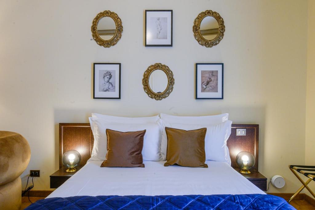 Neatly made bed with white linens, two brown pillows, framed black-and-white artwork and ornate gold mirrors hung above, and modern bedside lamps.