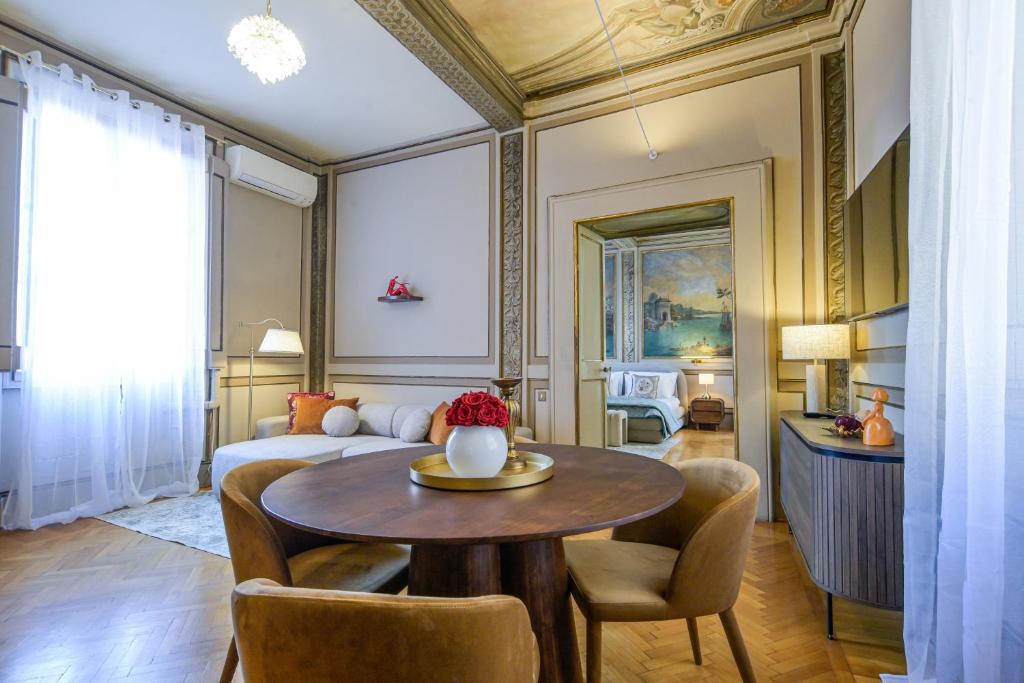 Elegant living room with a round wooden table, beige chairs, a white sofa, and an open door revealing a bedroom with a mural.