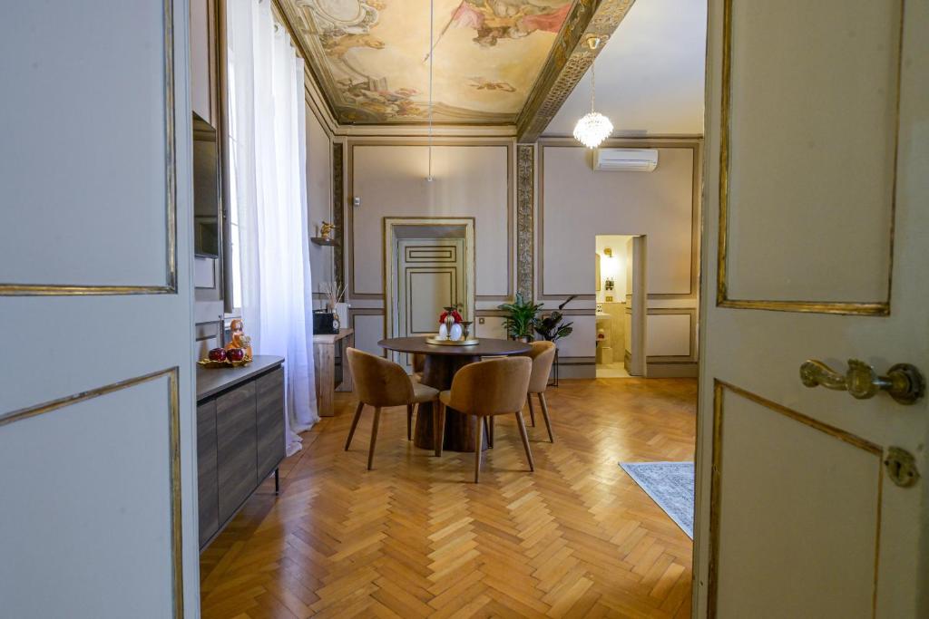 Elegant dining room with round wooden table, four brown upholstered chairs, ornate ceiling painting, and parquet floor.