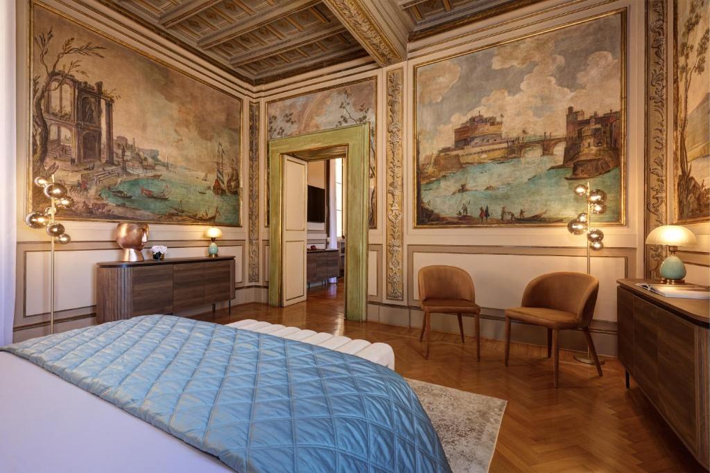 Luxurious bedroom with parquet flooring, large paintings on walls, two brown chairs, wooden dressers, and a blue quilted bedspread.